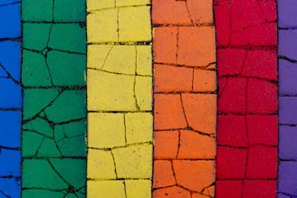 A series of cracked tiles arranged in vertical columns, each painted in a different vibrant color including blue, green, yellow, orange, red, and purple.