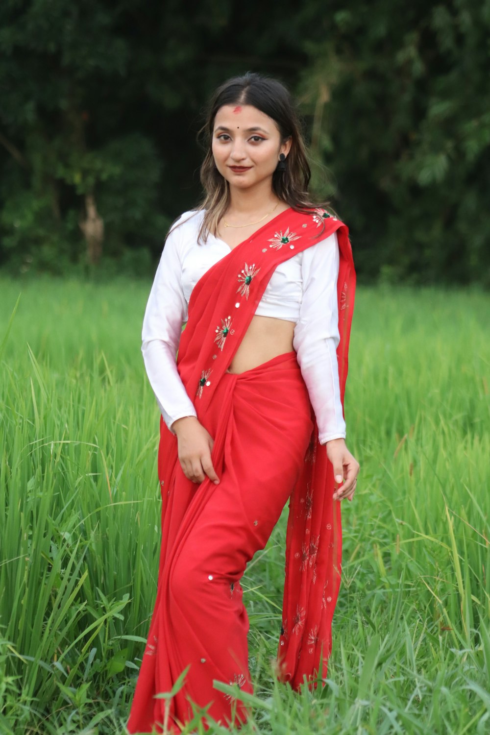 a woman in a red sari standing in tall grass
