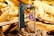 A smartphone is positioned against a backdrop of wooden debris and leaves. The screen displays a colorful card game card. The phone is angled to show both the front screen and the back camera. The surrounding environment includes fragments of wood and autumn leaves.