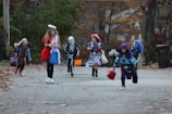 Children in costumes trick-or-treating around festival booths decorated for Halloween.