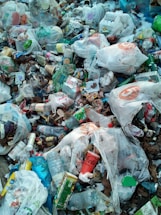 A pile of mixed garbage consisting mostly of plastic bags, bottles, containers, and various packaging materials. The litter is scattered widely with noticeable brands visible on some items. There is a mix of colors and textures among the waste, creating a cluttered and chaotic appearance.