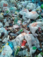 A pile of mixed garbage consisting mostly of plastic bags, bottles, containers, and various packaging materials. The litter is scattered widely with noticeable brands visible on some items. There is a mix of colors and textures among the waste, creating a cluttered and chaotic appearance.