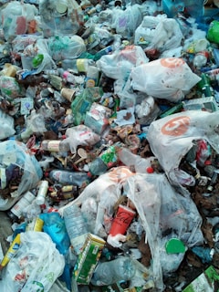 A pile of mixed garbage consisting mostly of plastic bags, bottles, containers, and various packaging materials. The litter is scattered widely with noticeable brands visible on some items. There is a mix of colors and textures among the waste, creating a cluttered and chaotic appearance.