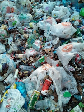 A pile of mixed garbage consisting mostly of plastic bags, bottles, containers, and various packaging materials. The litter is scattered widely with noticeable brands visible on some items. There is a mix of colors and textures among the waste, creating a cluttered and chaotic appearance.