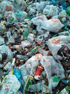 A pile of mixed garbage consisting mostly of plastic bags, bottles, containers, and various packaging materials. The litter is scattered widely with noticeable brands visible on some items. There is a mix of colors and textures among the waste, creating a cluttered and chaotic appearance.