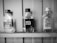 Three empty glass bottles with labels are displayed on a wooden shelf. They include branding in various languages, with prominent text and design elements indicating different vodka brands.