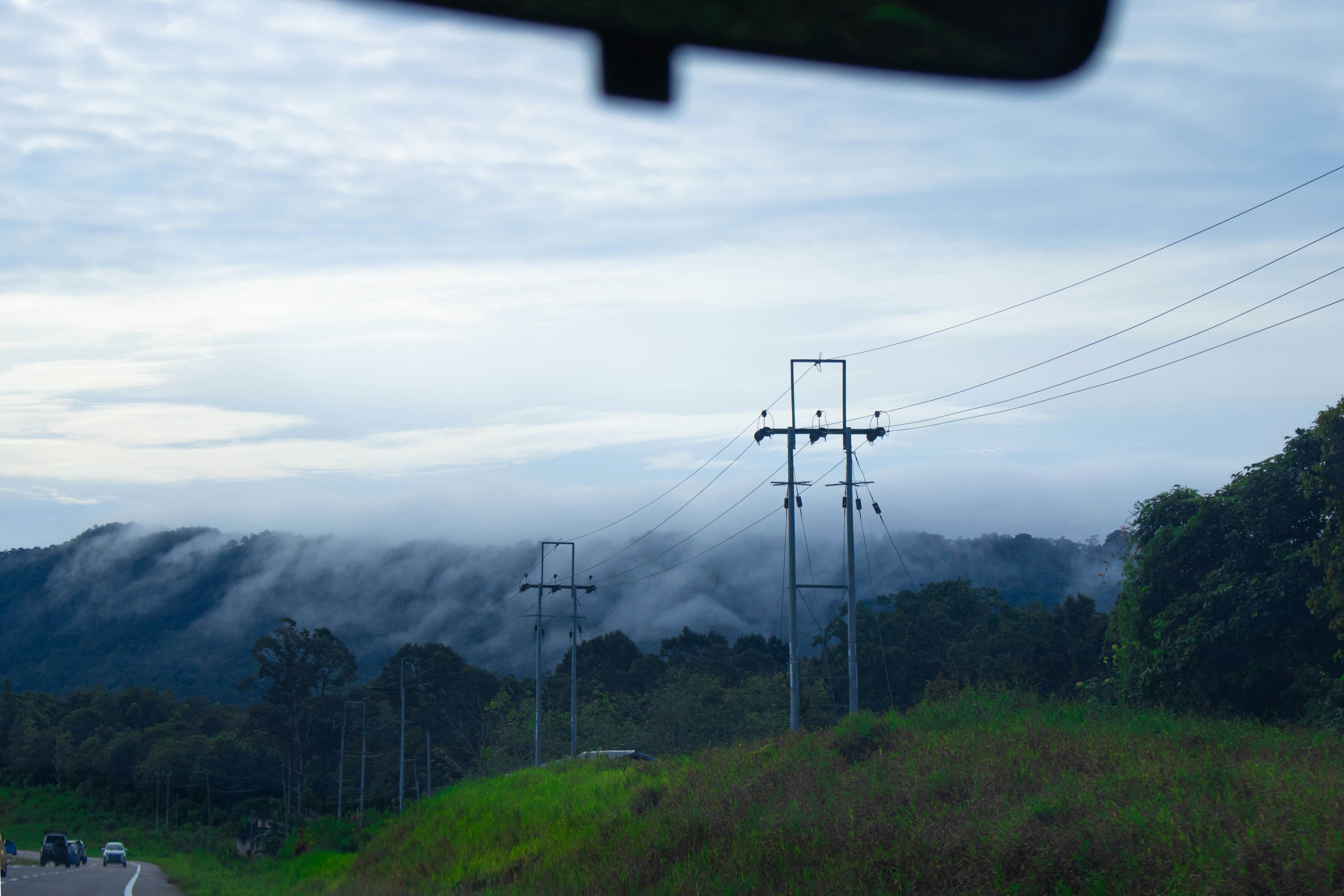 Power lines running through dark forested mountain terrain, overcast moody sky, deep greens and grays, no flames