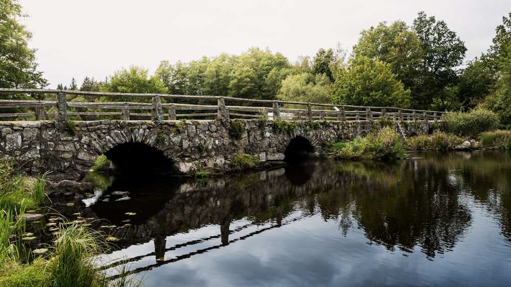 a stone bridge over a river with a wooden fence