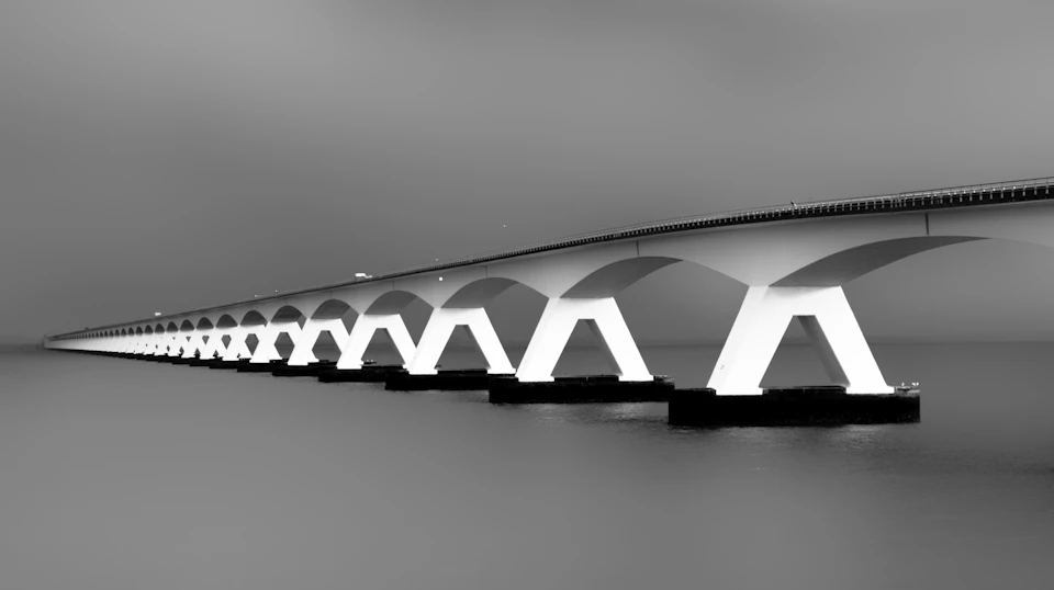 Long, white bridge spanning across water with multiple arches and supports in black and white