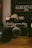 A vintage camera is prominently displayed on a wooden surface, surrounded by other camera equipment and accessories. In the background, a poster or book reads 'Albertville 1992' with some French text, suggesting an Olympic event theme. The setting conveys a nostalgic, analog atmosphere.