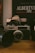 A vintage camera is prominently displayed on a wooden surface, surrounded by other camera equipment and accessories. In the background, a poster or book reads 'Albertville 1992' with some French text, suggesting an Olympic event theme. The setting conveys a nostalgic, analog atmosphere.