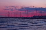 Silhouetted sails against a vibrant pink and purple sky at dusk.