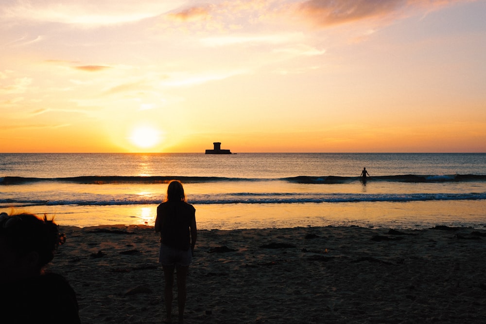 a woman standing on top of a sandy beach next to the ocean