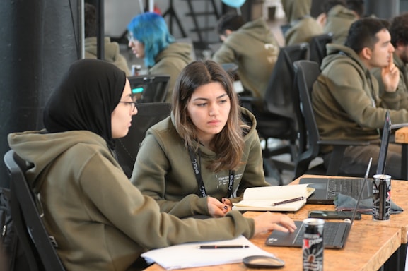 Two young adults collaborating over laptops in a cozy workspace filled with plants and tech gadgets.