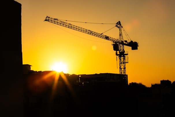 Sunset view of a construction crane silhouetted against the orange sky.