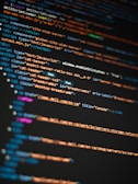 Colorful lines of HTML and JavaScript code are displayed on a computer screen, highlighted in different colors to differentiate elements, attributes, and text.