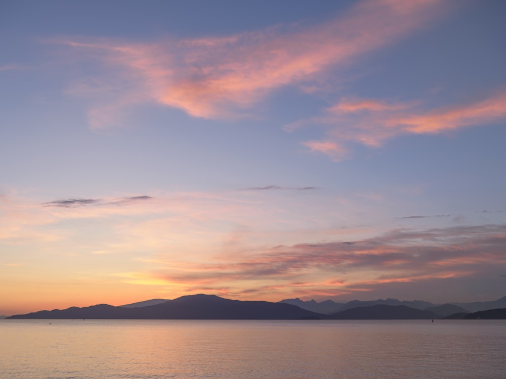 a beautiful sunset over the ocean with mountains in the distance