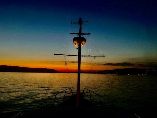 A calm sea horizon at sunset with a silhouette of a ship's mast.