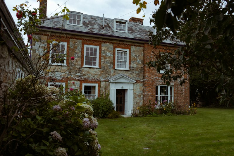 Stone and brick farmhouse with sash windows, hydrangeas and a lawn
