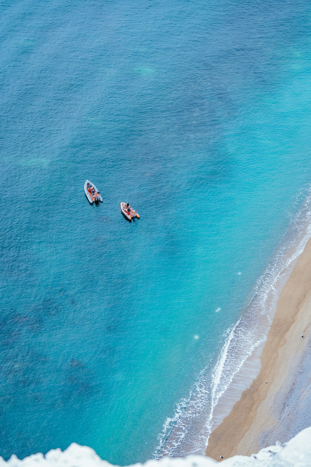 two boats floating on the ocean near a sandy beach