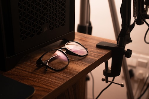 A pair of sleek smartglasses resting on a wooden desk beside a laptop.