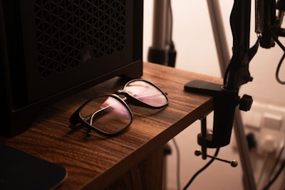 Close-up of blue light blocking glasses resting on a wooden desk with a laptop in the background.