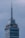 A tall skyscraper with an antenna at the top, featuring a digital clock displaying the same time on two sides. The building has several floors, with a section labeled 'LATINO SEGUROS'. The sky is overcast, giving a greyish backdrop.