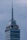 A tall skyscraper with an antenna at the top, featuring a digital clock displaying the same time on two sides. The building has several floors, with a section labeled 'LATINO SEGUROS'. The sky is overcast, giving a greyish backdrop.