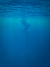 A dynamic shot of a scuba diver illuminated by rays of light filtering through a dark underwater cave.