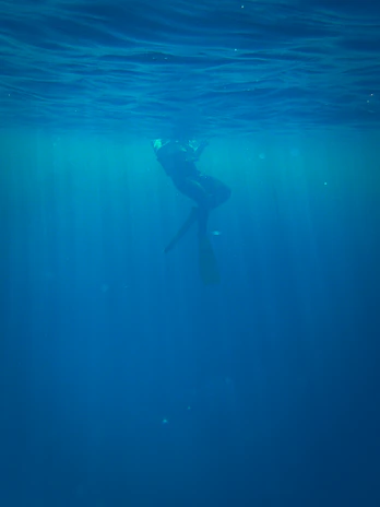 A dynamic shot of a scuba diver illuminated by rays of light filtering through a dark underwater cave.