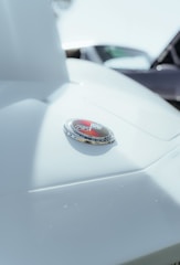 Close-up of a car hood emblem with a triangular logo and chrome accents. The image is focused on the shiny badge, emphasizing the sleek design and details.