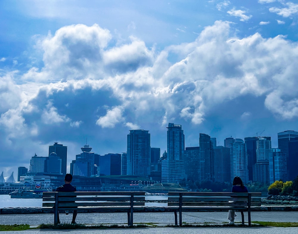 two people sitting on a bench in front of a city