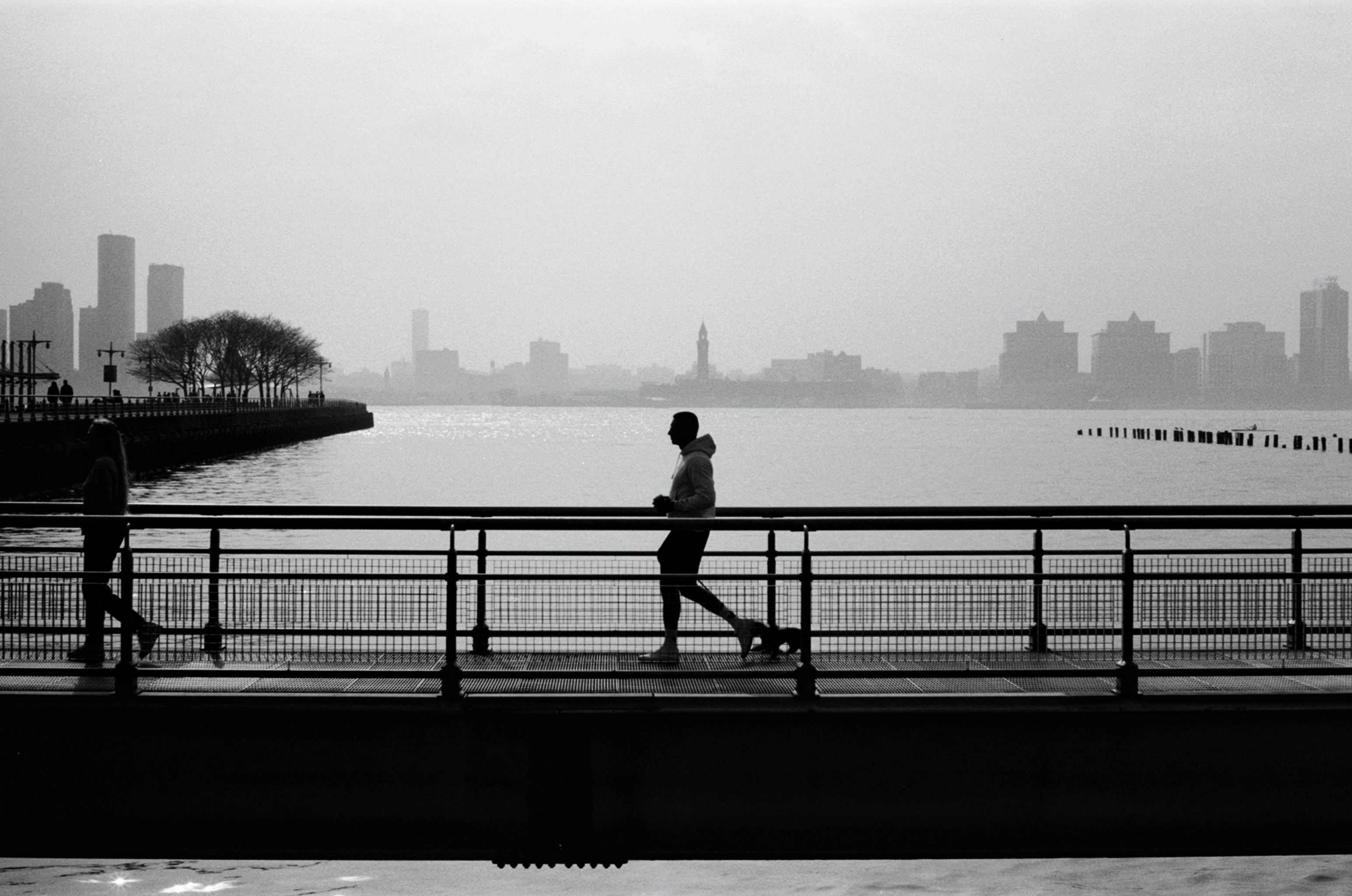 Side profile silhouettes of community runners on a bridge path at sunrise, atmospheric fog, city skyline background, motion and emotion