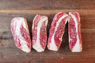 Four slices of raw beef are seasoned with salt and pepper, arranged on a wooden cutting board. The marbling of the meat is prominently visible.