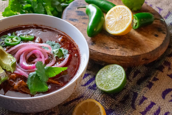A steaming bowl of homemade Mexican pozole garnished with radishes and lettuce.