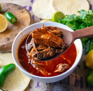 a spoon full of chili sauce with tortillas and limes in the background