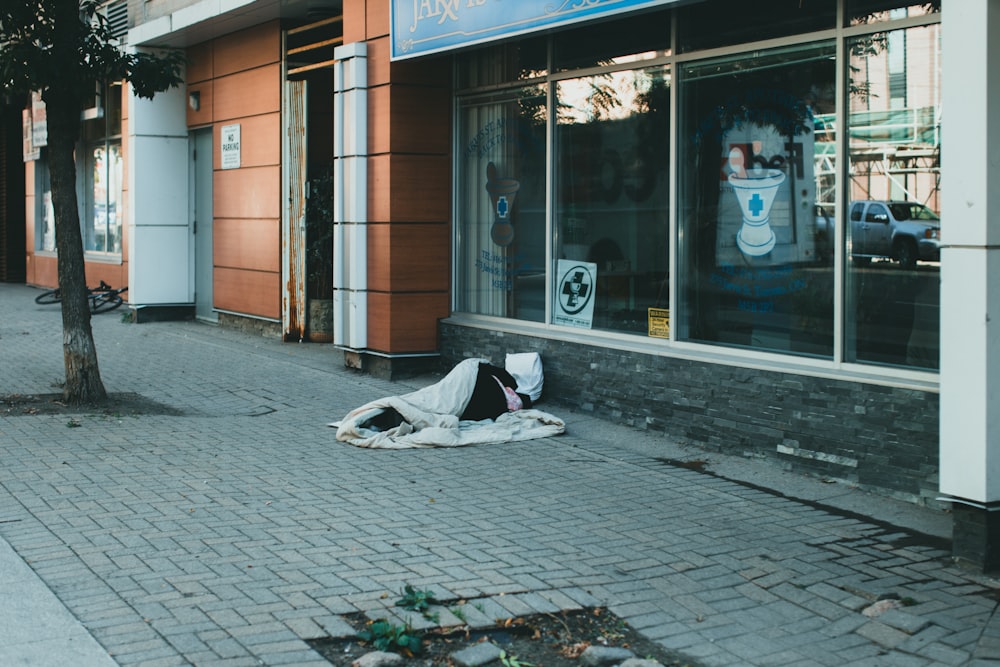 a homeless person sleeping on the sidewalk in front of a store