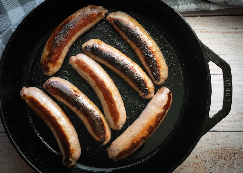 five sausages are cooking in a cast iron skillet