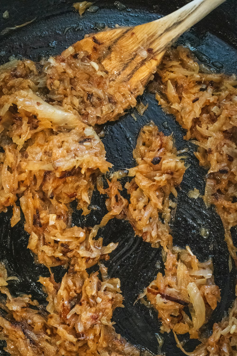 a frying pan filled with fried food and a wooden spoon