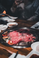 Chef carefully placing thin slices of beef on the grill, flames flickering beneath.