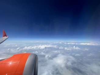 An airplane wing and engine are visible against a backdrop of a clear blue sky and scattered white clouds.