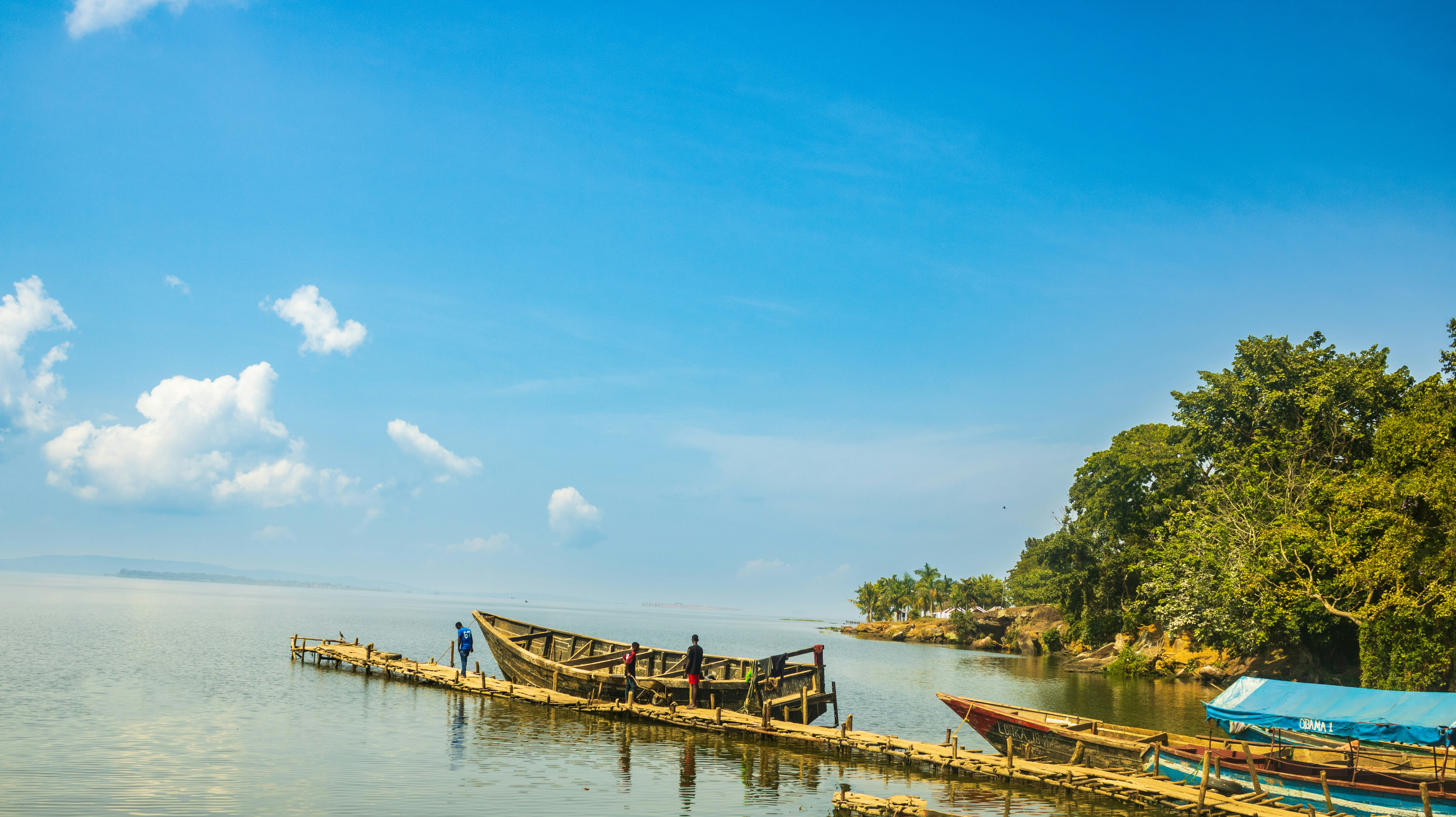 A panoramic shot of Lake Bunyonyi in Uganda at sunrise, with golden light and mist rising from the water.