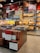 A retail display features a variety of packaged baked goods, including mooncakes and other traditional pastries. The packages are neatly stacked on shelves and tables, with some boxes showcasing intricate designs. Signage in a language possibly indicating product names and prices is visible. The display is well-lit, highlighting the vibrant packaging and colorful product boxes.