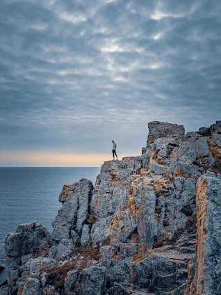 A traveler standing on a cliff edge watching the sunrise over the ocean, embodying adventure and exploration.