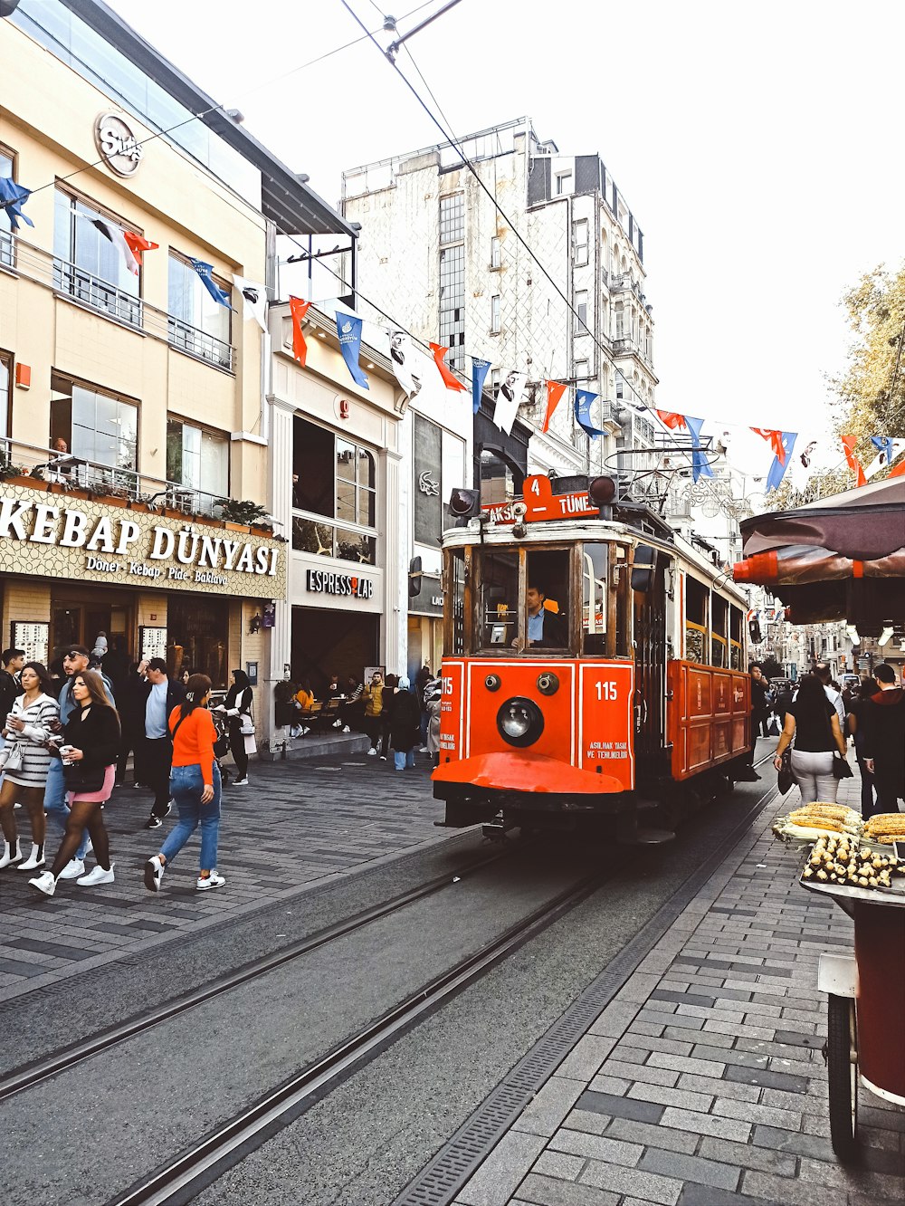 a red trolley driving down a street next to tall buildings