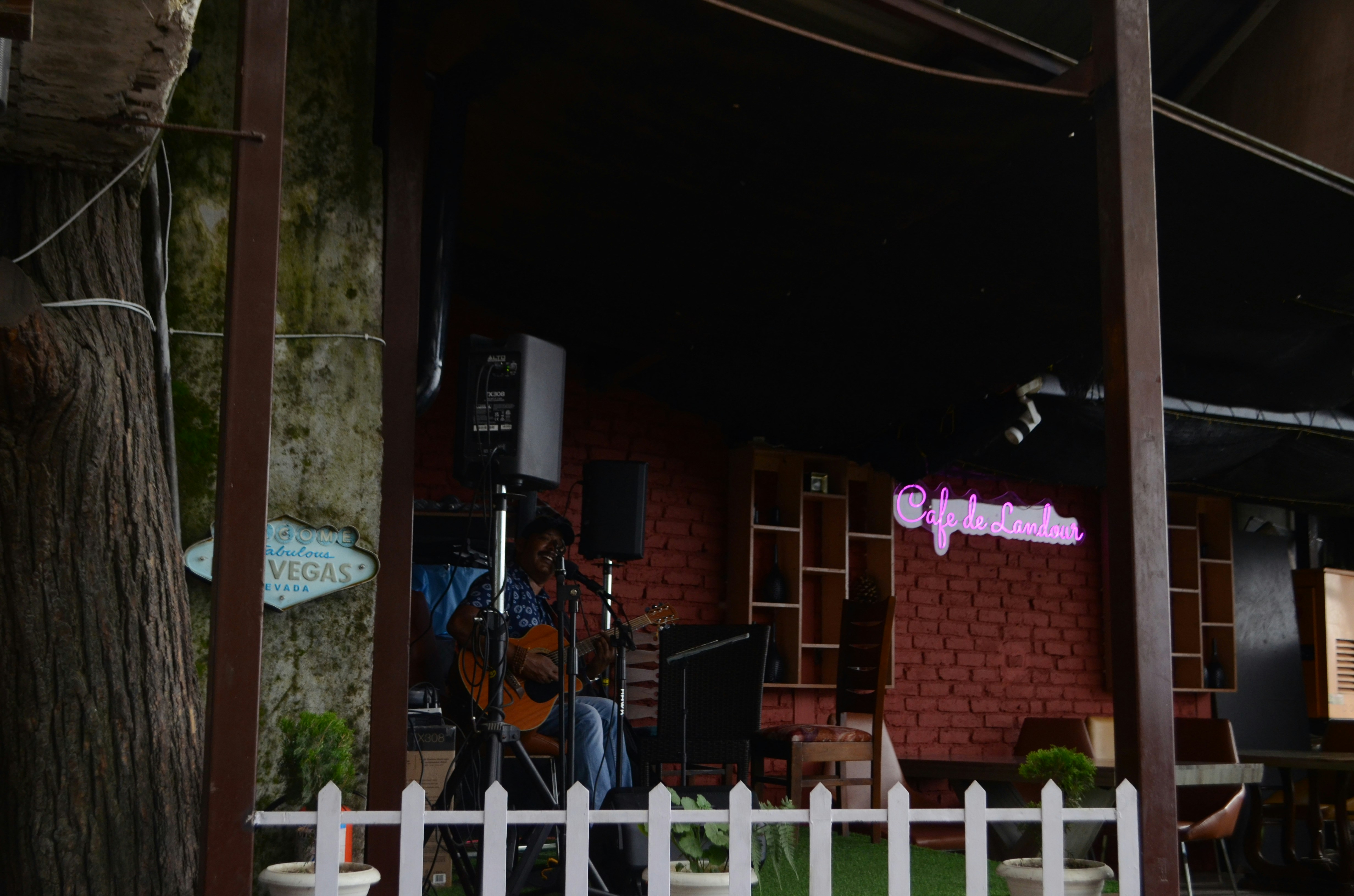 a man playing a guitar in front of a white fence