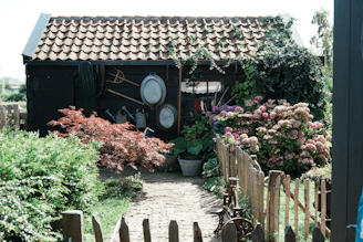 A rustic wooden shed surrounded by blooming herbs and garden tools.