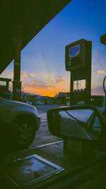 Fuel delivery truck unloading gasoline at a busy service station during sunset.