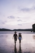 A couple walking hand in hand along a beach at dusk.