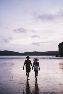 A couple walking hand in hand along a beach at dusk.